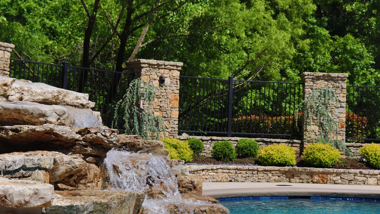 Natural-stone water feature and stone pillar wall beside a backyard pool