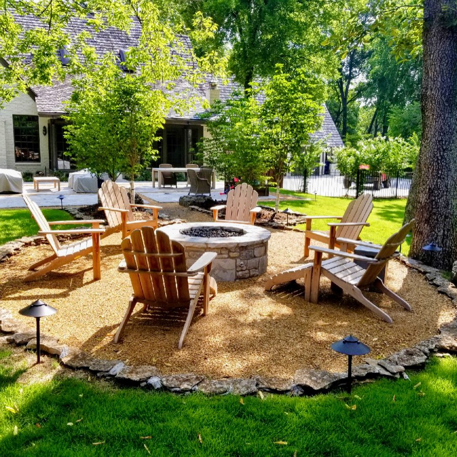 Stone fire-pit surrounded by a mulched hardscape seating area under mature trees
