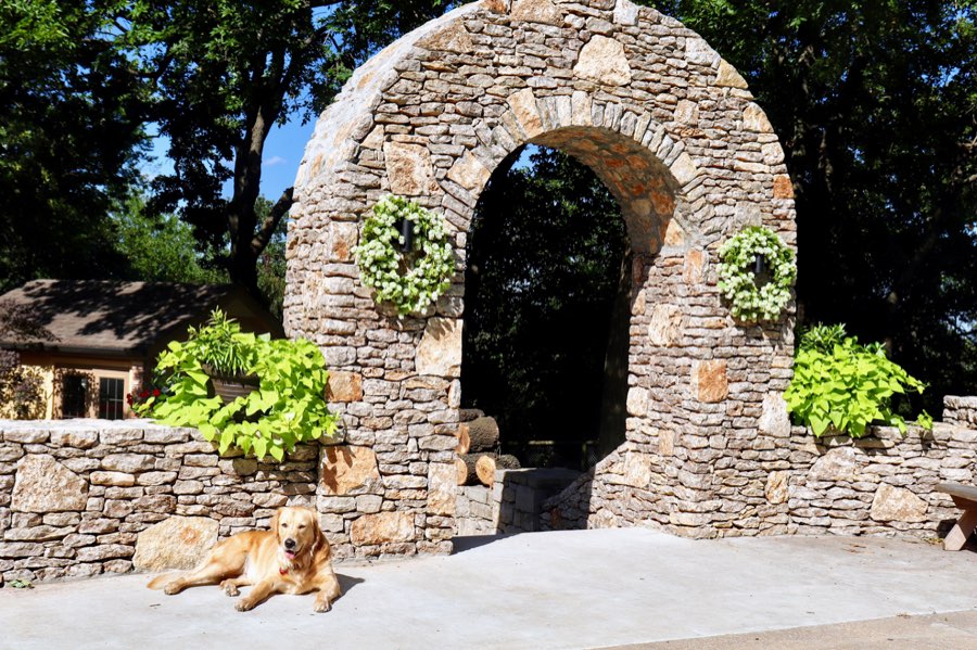 Hand-laid stone archway feature with a low stone wall and a concrete patio